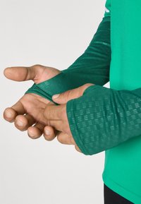 Zöld, hosszú ujjú ing texturált anyagból, hüvelykujjtartókkal a mandzsettáknál és sima, testhezálló fazonnal a sportos viselethez.