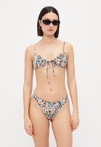 Blommigt bikini-set med en knyt-föran topp med justerbara axelremmar och matchande lågmidjade trosor. Färgerna inkluderar rosa, grön och blå. Slät textur.