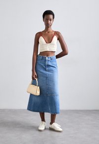 Top court au crochet crème avec des accents rouges. Jupe maxi en denim taille mi-haute. Baskets blanches et petit sac à main beige.