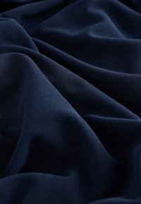 Tengerészkék színű szövet, puha, sima textúrával, lágyan hullámzó redőkkel és finom kötésmintával. Kiválóan alkalmas különféle textilalkalmazásokhoz.