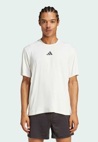 Weißes kurzärmliges Sportshirt mit rundem Hals und subtiler Textur, mit einem dunklen Logo auf der Brust und lockerer Passform.