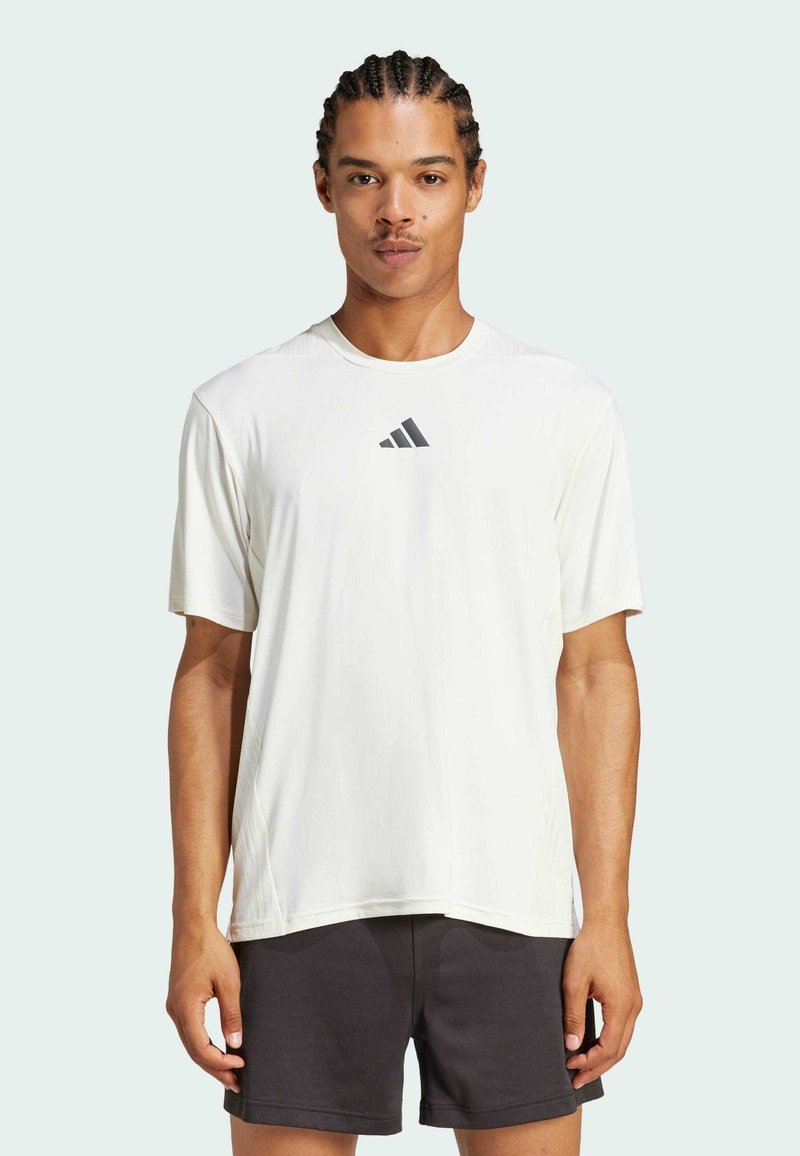 Weißes kurzärmliges Sportshirt mit rundem Hals und subtiler Textur, mit einem dunklen Logo auf der Brust und lockerer Passform.