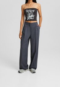 Grå rutiga byxor med vida ben och veck, i kombination med en svart tube-top med grafiskt tryck. Grå och vita sneakers fulländar looken.