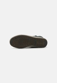 Black shoe with textured rubber sole, featuring zigzag patterns. Material appears durable, with a slight sheen and low-profile design.