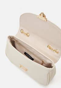 Kermaankeltainen käsilaukku, jossa on sileä pinta, kullanväriset metalliosat ja lukituspidike. Sisäpuolella on beige vuori ja vetoketjutasku.