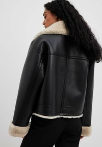 Sort læderjakke med falsk shearling krave og manchetter, der har en firkantet form og synlige syninger.