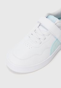Basket blanche avec accent bleu clair, bande Velcro et lacets sur un fond blanc uni, montrant les détails latéraux et supérieurs.