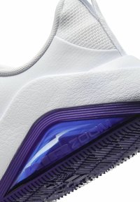 Zapatilla deportiva blanca con parte superior texturizada, detalles morados cerca de la suela y una unidad de amortiguación azul translúcida etiquetada como "AIR ZOOM".