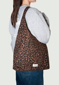 Leopardenmuster-Shopper-Tasche aus braunem und schwarzem Stoff mit weicher Textur. Breiter Träger und Etikett-Detail am unteren Rand.