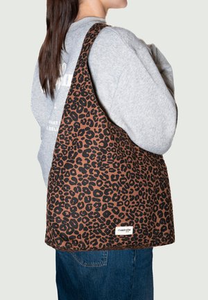 Sac cabas imprimé léopard en tissu marron et noir avec une texture douce. Large bandoulière et détail d'étiquette en bas.