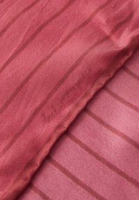 Tessuto trasparente di colore malva con sottili righe verticali. Texture liscia, aspetto leggero e testo del marchio appena visibile nel tessuto.