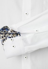 Biała koszula z teksturowanej tkaniny. Rękawy zdobione są kwiatowym wzorem w niebieskich i zielonych odcieniach, uzupełnionym o białe guziki.