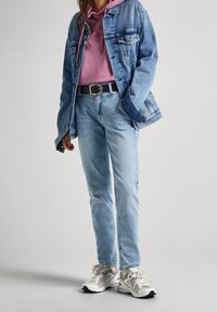 Chaqueta de mezclilla azul claro con dos bolsillos en el pecho, sudadera rosa, jeans azul claro, cinturón negro y zapatillas gris-blancas con acentos.
