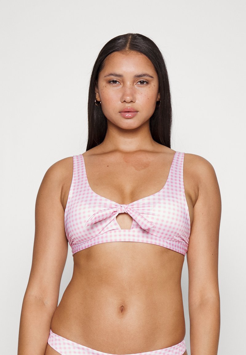 Top de bikini em padrão de gingham rosa e branco com detalhe de laço na frente, alças largas e recorte em forma de olho-chave. Tecido suave, design ajustado.