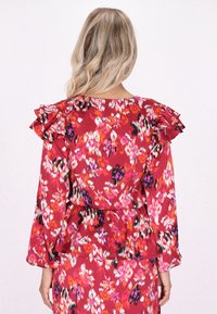 Blusa floreale rossa con maniche a balze, caratterizzata da un mix di motivi rosa, neri e bianchi. Tessuto morbido, vestibilità ampia e silhouette a peplo.
