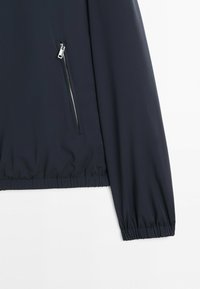 Marineblaue Jackenärmel mit elastischer Bündchenabschlusss und seitlicher, schräger Reißverschlusstasche, glattes Gewebe und minimale Nähte.