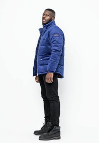 Vadderad marinblå jacka med hög krage och dragkedjestängning, med en slät yta och sidofickor. Svarta jeans och stövlar fulländar looken.