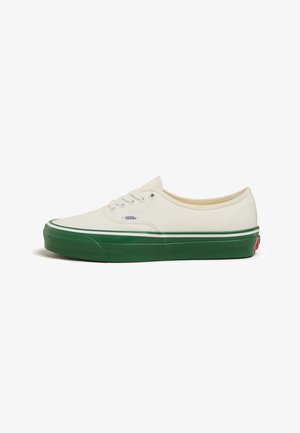Baskets en toile off-white avec semelle en caoutchouc verte, lacets blancs et logo discret. Présente une pointe arrondie et une bande verte contrastante.
