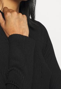 Schwarzer gerippter Strickpullover mit lockerem Schnitt, hoher Kragen und breiten Bündchen, der eine strukturierte Stoffdetail zeigt.