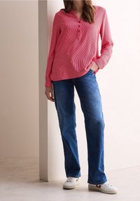 Long-sleeved, red and white striped shirt with a button placket, paired with blue straight-leg jeans and white sneakers with red accents.