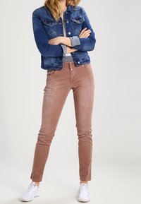 Jeansowa kurtka w ciemnoniebieskim kolorze z jasnoszarymi akcentami, w połączeniu z dopasowanymi jasnobrązowymi spodniami. Białe sneakersy dopełniają stylizację.