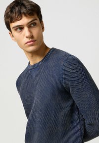 Marinblå, strukturerad stickad tröja med rund halsringning och ribbade detaljer. Har en tät väv med ett subtilt mönster och sidsprund.
