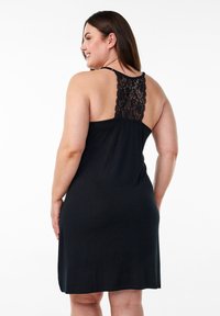 Abito nero realizzato in un tessuto leggero, con un pannello posteriore in pizzo e spalline regolabili. Design fino al ginocchio con una vestibilità comoda.