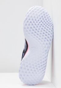 Zapatilla deportiva con una suela de goma blanca texturizada, parte superior de tela negra, acentos en rosa y azul, y un diseño de talón redondeado.