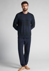 Tmavě modrá kostkovaná domácí souprava; tričko s dlouhým rukávem se zeleným károvaným vzorem a žebrovanými manžetami, doplněné elastickými kalhotami v pase. Měkká látka, pohodlný střih.