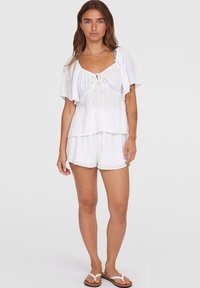 Witte top met korte mouwen en een strik voorkant, gecombineerd met bijpassende shorts. Lichtgewicht, gestructureerde stof met een gelaagd ontwerp. Slippers maken de look compleet.
