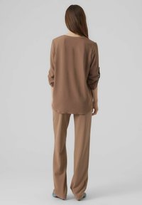 Top marrone con una vestibilità rilassata e maniche arrotolate, abbinato a pantaloni a gamba larga marroni coordinati. Tessuto liscio, design semplice, senza motivi visibili.