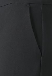 Pantaloni in tessuto nero con una texture liscia, forma slim-fit e dettagli di tasche nascoste. Il materiale è leggermente elasticizzato per garantire comfort.