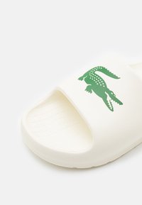 Sandale blanche à enfiler avec semelle intérieure texturée et logo crocodile vert sur la bride.