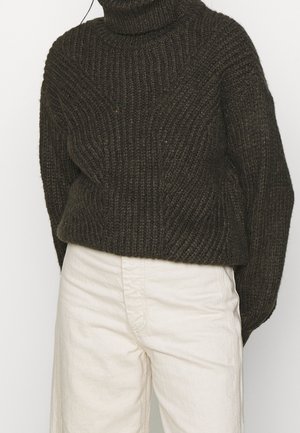 Tyk, mørkegrøn strikket sweater med høj hals og ribbet tekstur. Matchet med lette, cremede bukser i løs pasform.
