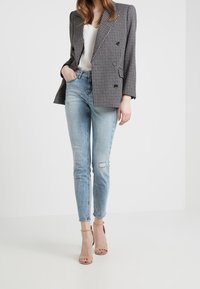 Dubbelknäppt grått hundtandsmönstrat blazer, vit topp, ljusblå skinny jeans med slitdetaljer och nudefärgade remsandaler.
