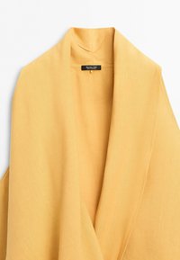 Yellow linen fabric draped to form a wide collar with a black label inside reading "Massimo Dutti Made in Portugal."