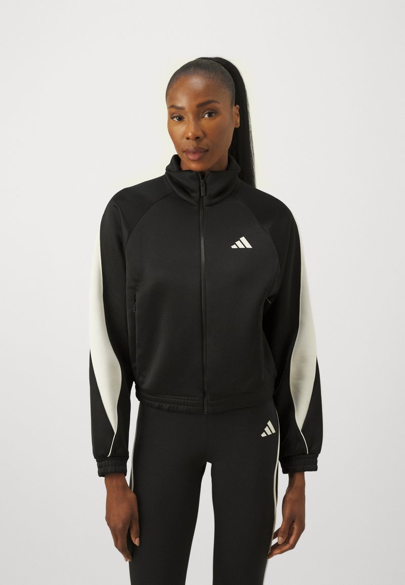 Giacca sportiva nera con colletto alto e chiusura con zip, con dettagli bianchi sulle maniche e il logo Adidas sul petto.