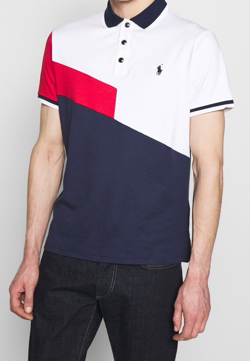 Polokošile s bílými, červenými a námořnickými barevnými bloky, námořnickým límcem a třemi černými knoflíky. Vyšívané logo na hrudi. K výrobě bylo použito bavlněné materiálu.