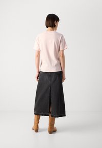 T-shirt di cotone rosa chiaro abbinato a una gonna di jeans nera con uno spacco sul retro e stivali marroni al ginocchio con un leggero tacco.