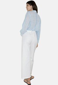 Chemise à rayures bleues à manches longues avec une coupe ample, associée à un pantalon large taille haute blanc et des sandales à lanières noires.