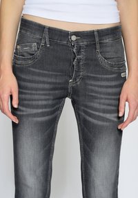 Svarta denimjeans med en åtsittande design, med framfickor, knappstängning och kontrasterande sömmar. Texturerad yta med urblekta mönster.