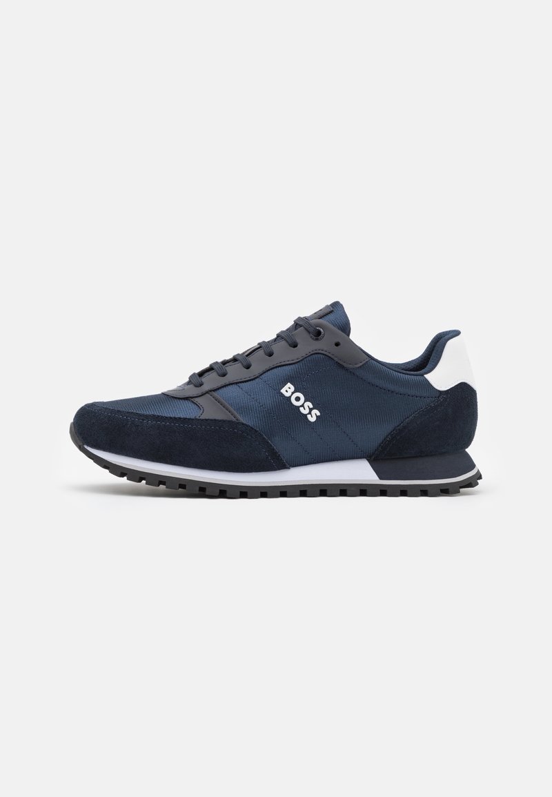 Chaussures de sport bleu marine avec panneaux en daim et nylon, présentant un accent blanc au talon, une semelle extérieure noire et un logo sur le côté.