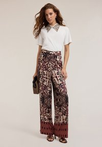 Witte korte mouw top met versierde kraag, gecombineerd met gebloemde, wijde broek in crème, bordeauxrood en donkere bloemenpatronen.