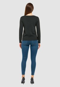 Maglione nero a maniche lunghe con scollatura a barca, abbinato a jeans blu aderenti e scarpe con tacco nere, mostrato da dietro.