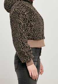 Sudadera corta con estampado de leopardo marrón y negro, de una tela suave y texturizada, y con un bolsillo tipo canguro. Puños y bajo ajustados en color liso.
