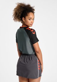 Sportoutfit med en grå topp med korta ärmar och svarta mönstrade ärmar samt orange accenter, kombinerad med en grå kjol med elastisk midja.