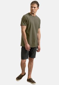 T-shirt in cotone verde oliva con maniche corte, abbinato a pantaloni corti in denim scuro. Sneakers marroni completano il look informale. Design semplice e pulito.