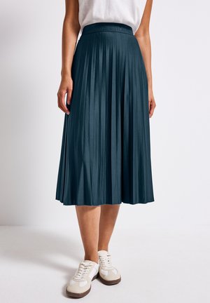 Dark teal pleated midi skirt with a smooth texture and a waist band. Paired with white sneakers featuring beige and dark accents.