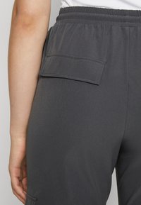 Harmaat cargo-housut, joissa on teksturoitu, kevyt kangas. Ominaisuuksiin kuuluu joustava vyötärö ja takakujettaja, jossa on läpällä varustettu tasku.