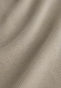 Nahaufnahme eines beigen, gerippten Stoffs mit weichen Falten, die ein strukturiertes, wellenförmiges Muster und subtile Schatten bilden.